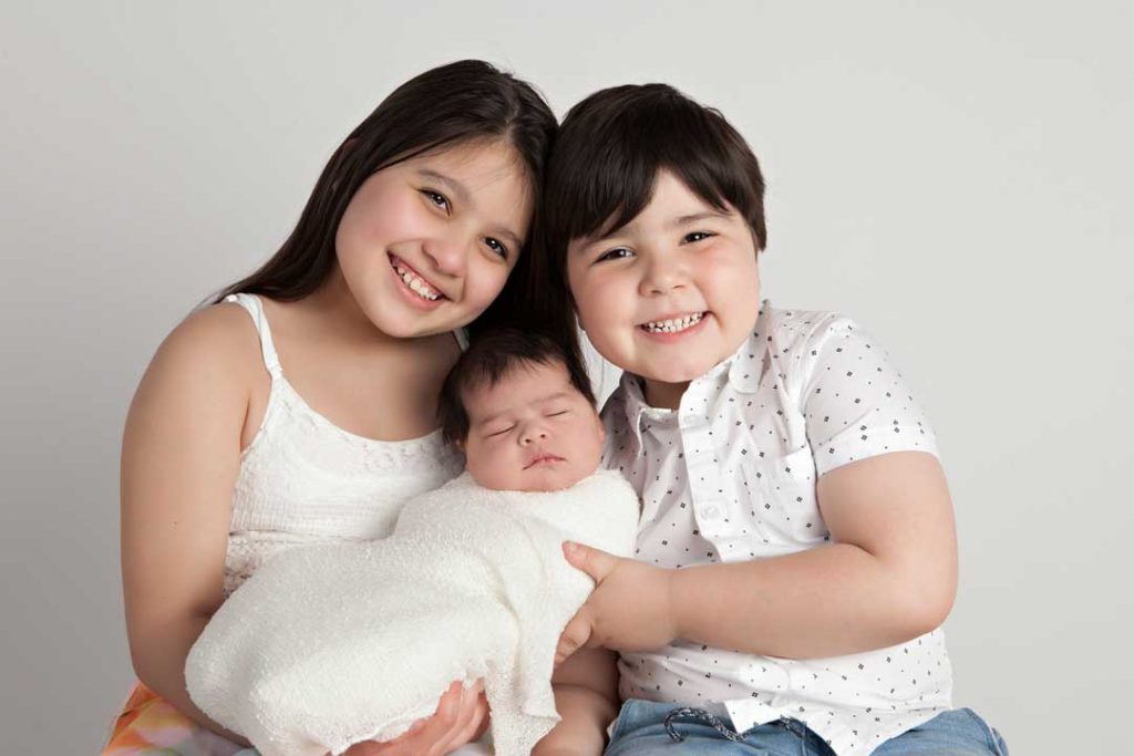 Newborn being held by sibling smiling at camera.Newborn photography melbourne