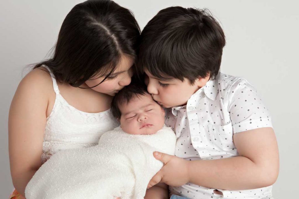 Siblings kissing newborn.