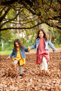 two girls holding hands kicking Autumn Leaves