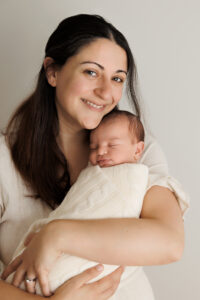 Mum holding Newborn looking and smiling at the camera, In-Home Newborn Photography in Aintree
