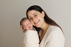 Mum holding Newborn looking and smiling at the camera, In-Home Newborn Photography in Aintree