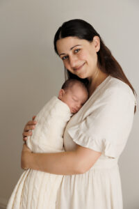 Mum holding Newborn looking and smiling at the camera, In-Home Newborn Photography in Aintree