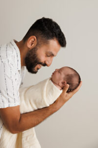Dad and Newborn looking down and smiling at his newborn daughter, In-Home Newborn Photography in Aintree