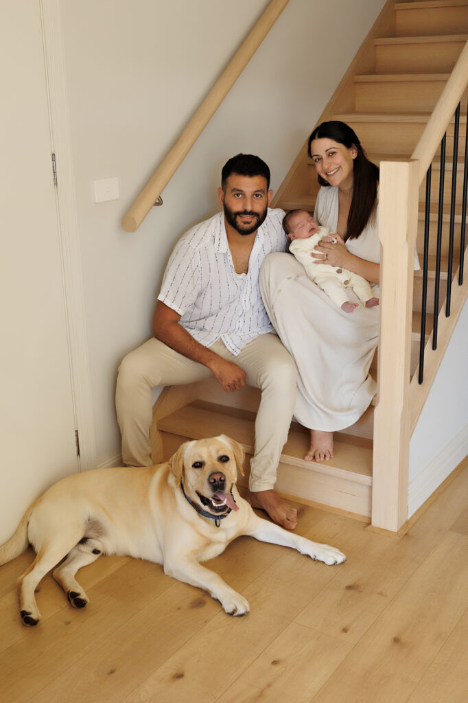 parents and newborn and family dog sitting in stairwell In-Home Newborn Photography in Aintree